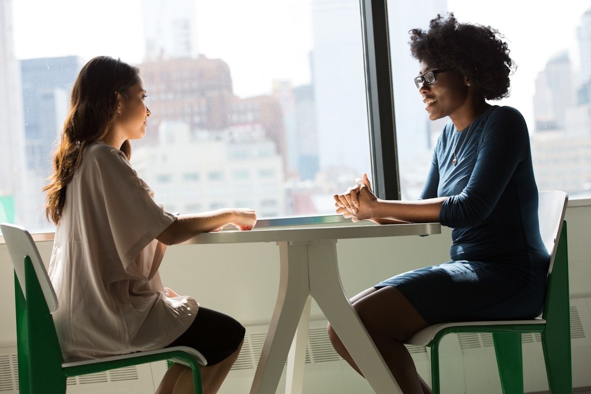 Two colleagues in conversation across a table by a city window